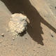 The rust-orange surface of Mars, with a large rock next to the wheel of Perseverance.
